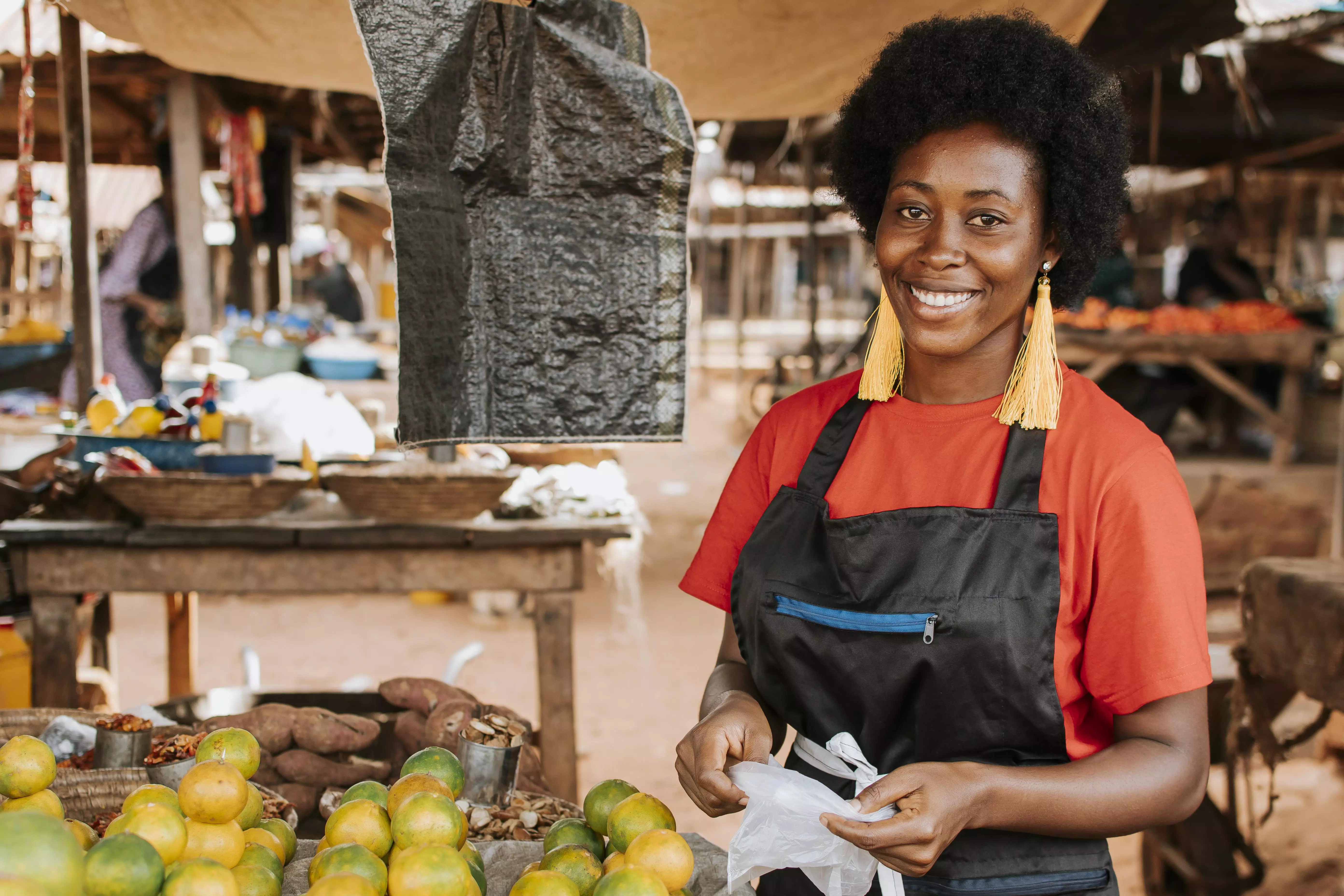 lady in a market standing next to a stall selling vegetables